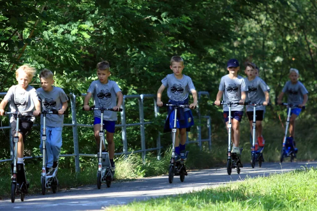 Uczestnicy jadą na hulajnogach w plenerze